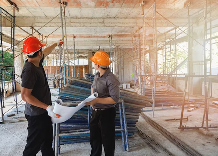 Two construction workers with hard hats discussing plans at a construction site.